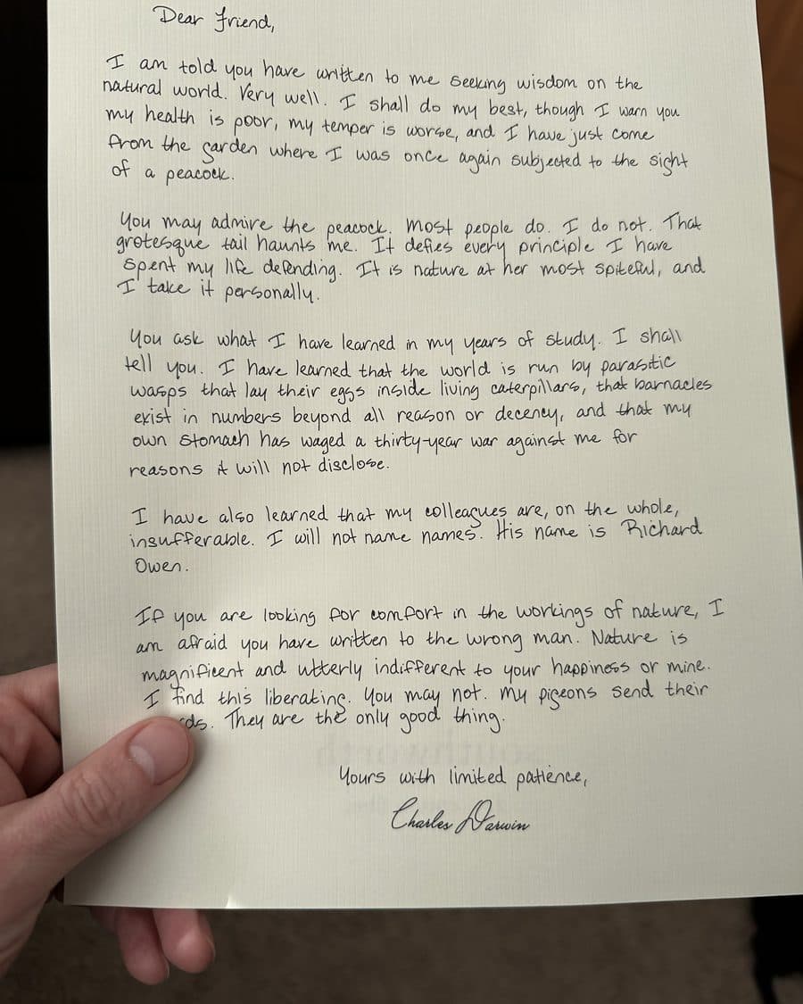 A handwritten letter from Charles Darwin on cream paper, held in a reader's hand